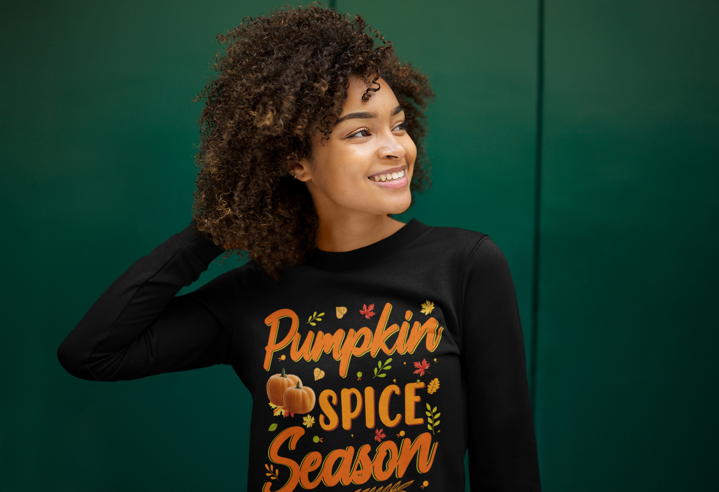 A woman wearing a black Pumpkin Spice Season Sweatshirt by Sharp Tact Kreativ embraces the fall vibes.