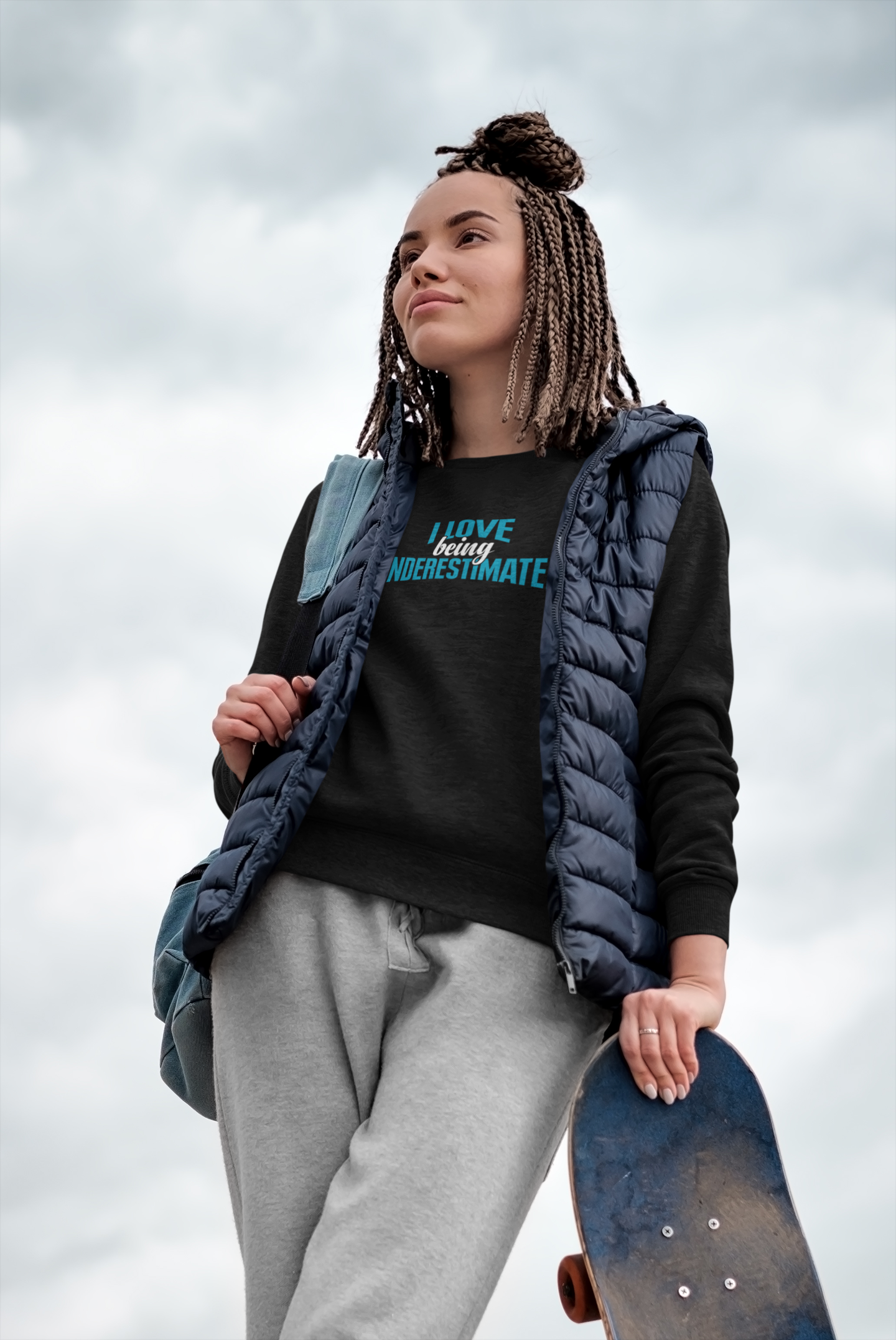 A woman holding a skateboard and wearing the I Love Being Underestimated Sweatshirt by Sharp Tact Kreativ | Tees & Gifts with Encouraging Messages to Brighten Your Day with a Bit of Wit.