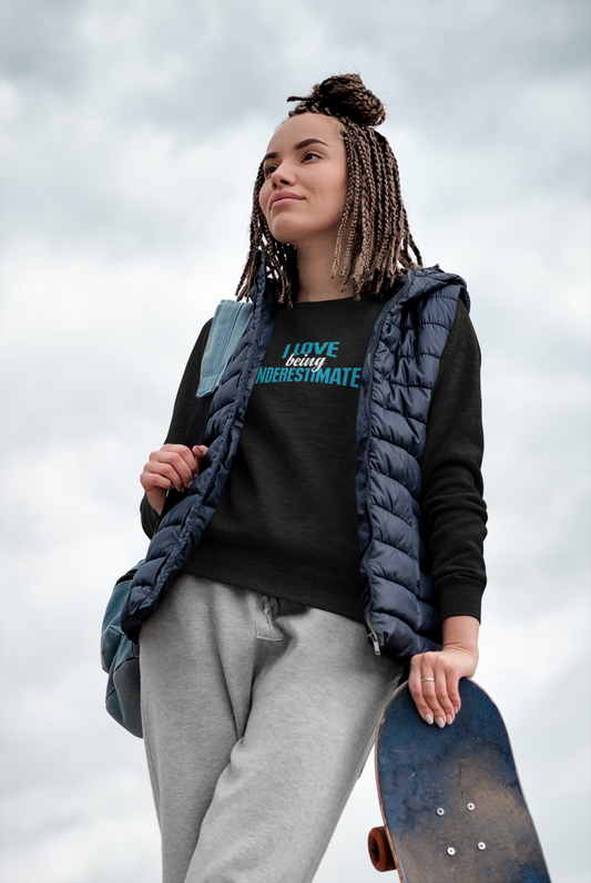 A woman holding a skateboard and wearing the I Love Being Underestimated Sweatshirt by Sharp Tact Kreativ | Tees & Gifts with Encouraging Messages to Brighten Your Day with a Bit of Wit.