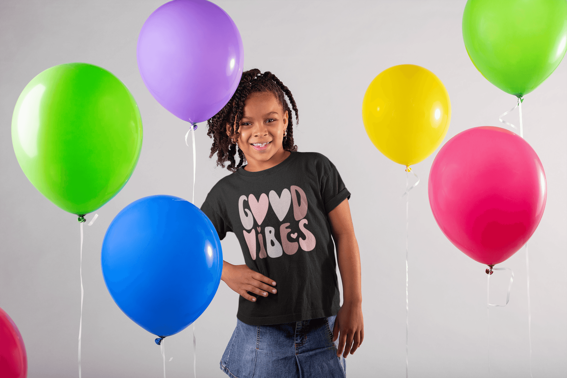 A little girl standing in front of balloons with the Sharp Tact Kreativ Good Vibes Tee (Youth Size).