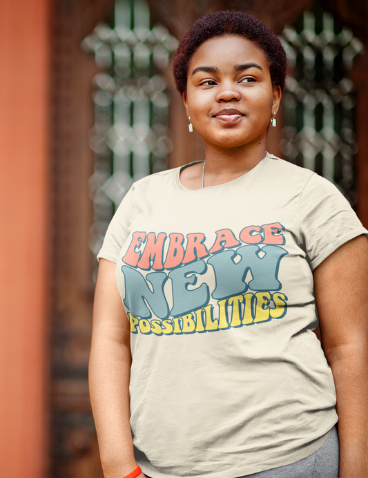 A person stands in front of a decorative background, wearing the Sharp Tact Kreativ Embrace New Possibilities Tee that reads "Embrace New Possibilities," showcasing a bold design that highlights new opportunities.