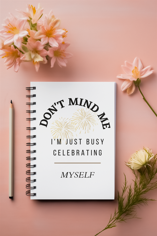 A Don't Mind Me Notebook by Sharp Tact Kreativ | Tees & Gifts with Encouraging Messages to Brighten Your Day with a Bit of Wit displays the message "Don't mind me, I'm just busy celebrating myself," surrounded by flowers and a pencil on a pink surface.
