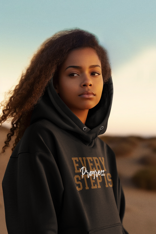 A young woman wearing a black Sharp Tact Kreativ hoodie with the words 'every step' written on it, showcasing the Every Step is Progress Hoodie design.
