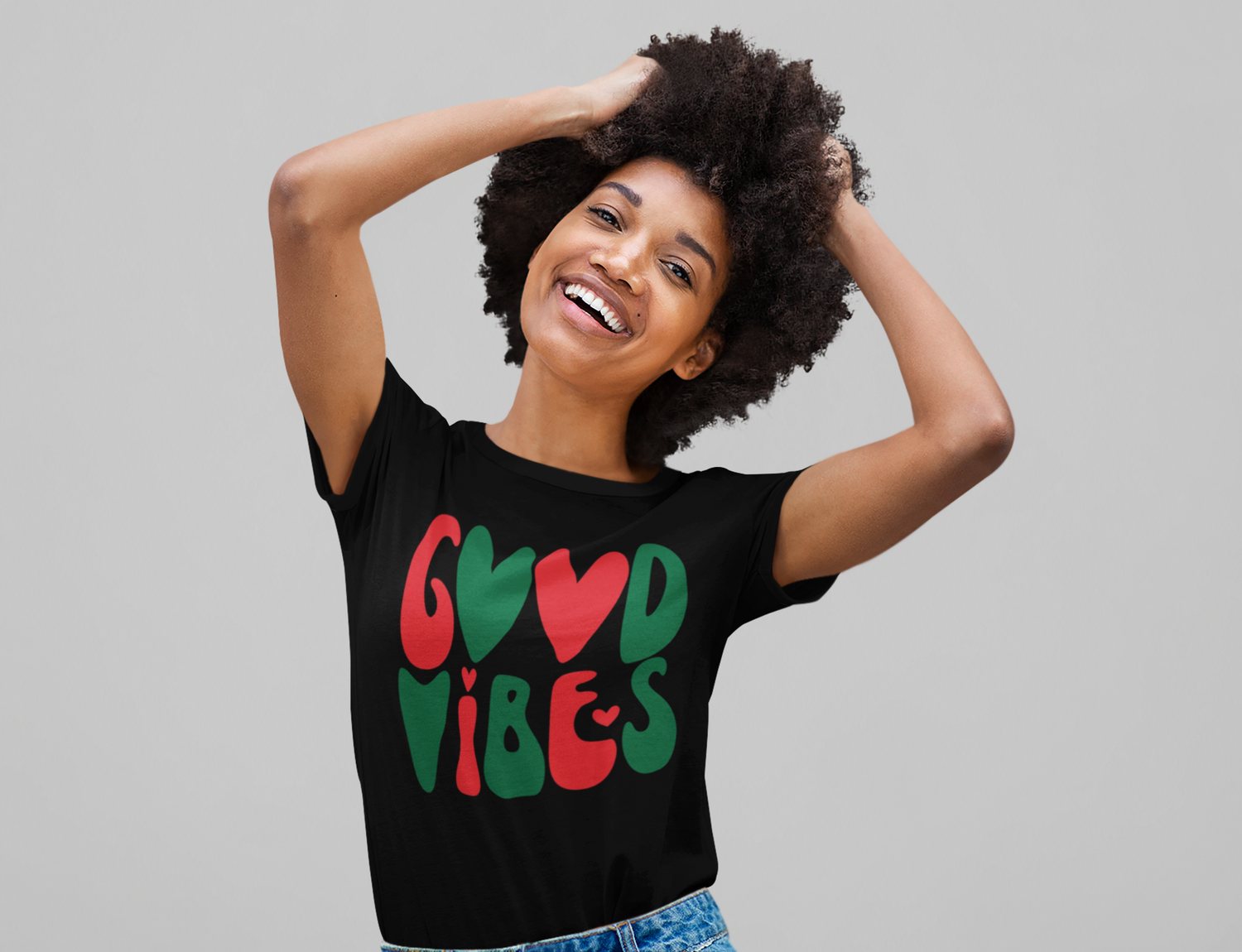 A person is smiling with hands on head, wearing the Good Vibes Holiday Tee by Sharp Tact Kreativ. This unisex black t-shirt is crafted from ring-spun cotton and features "Good Vibes" in bold red and green letters.