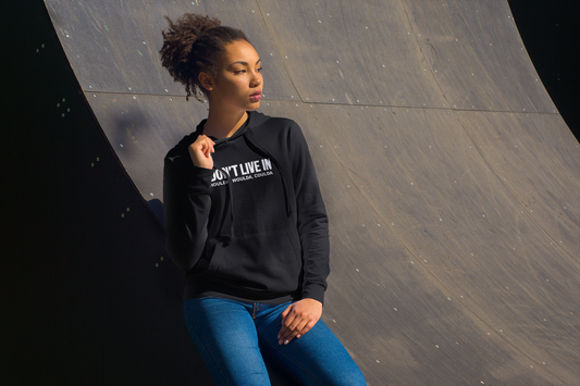 A woman exuding comfort and confidence as she leans against a skateboard ramp, wearing the Sharp Tact Kreativ I Don't Live in Shoulda, Woulda, Coulda Hoodie.