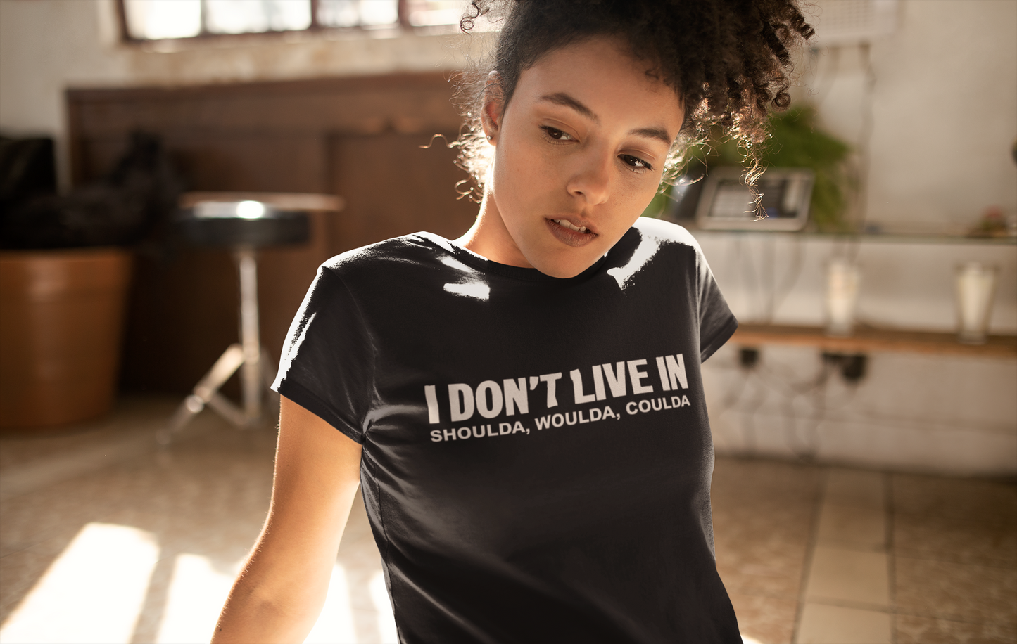 A woman wearing a black t-shirt that says I Don't Live in Shoulda, Woulda, Coulda Tee by Sharp Tact Kreativ | Tees & Gifts with Encouraging Messages to Brighten Your Day with a Bit of Wit.