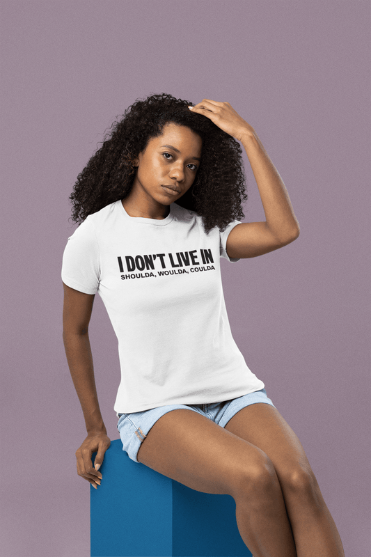 A woman wearing a white t-shirt that says "I Don't Live in Shoulda, Woulda, Coulda Tee" by Sharp Tact Kreativ | Tees & Gifts with Encouraging Messages to Brighten Your Day with a Bit of Wit.