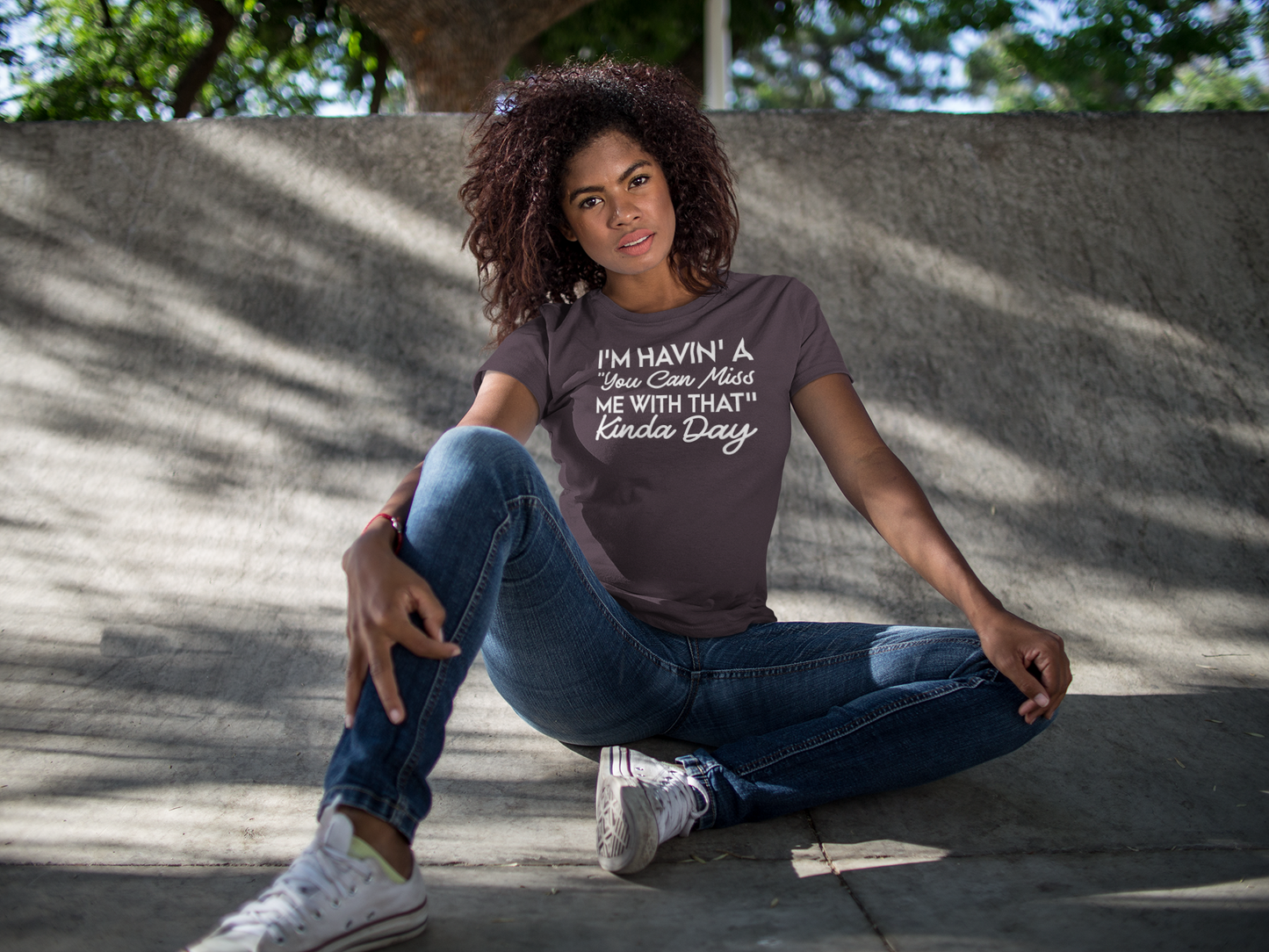 A woman sitting on a skateboard wearing the Sharp Tact Kreativ | Tees & Gifts with Encouraging Messages to Brighten Your Day with a Bit of Wit's "I'm Havin' A "You Can Miss Me With That" Kinda Day Tee" gray t-shirt.