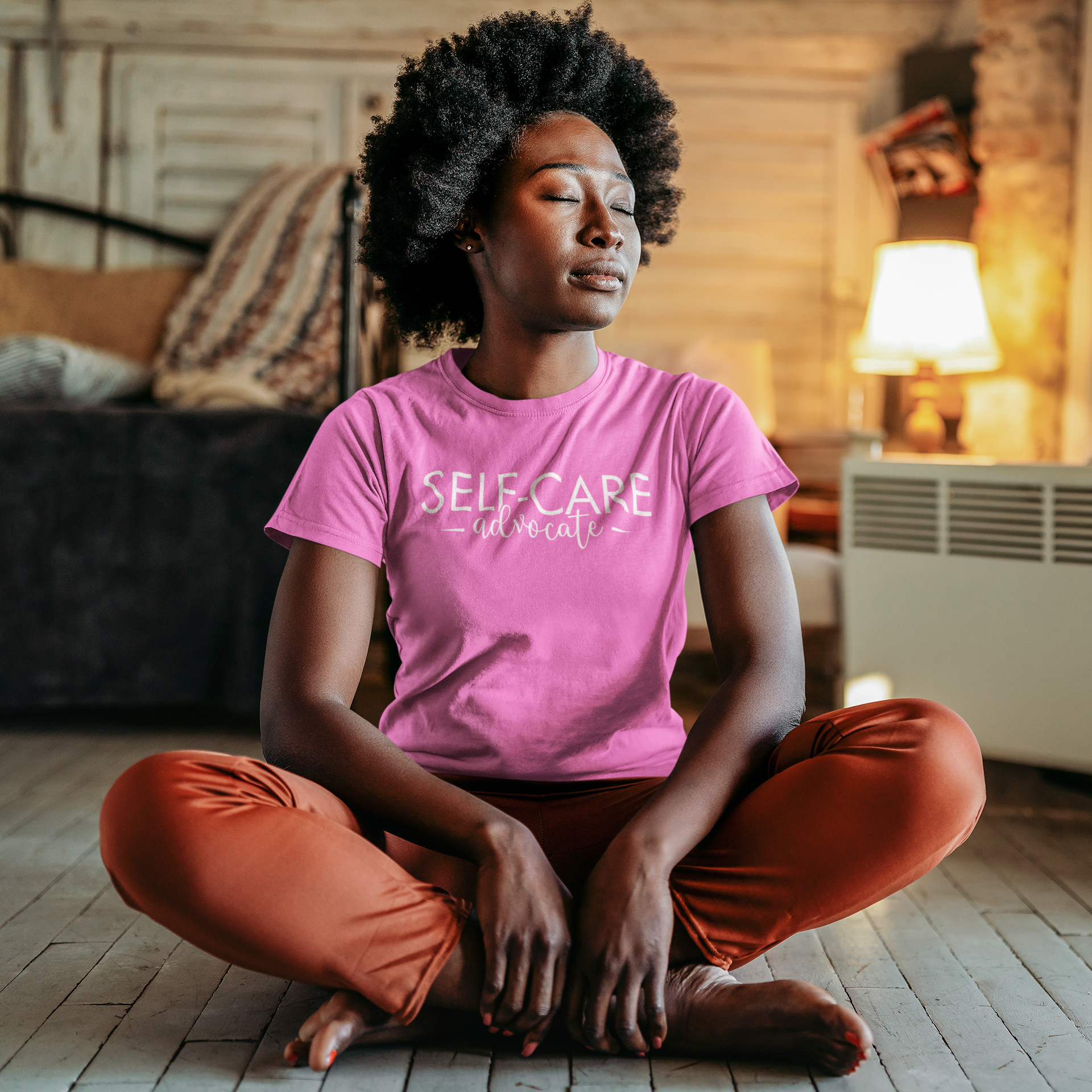 A woman sitting on the floor wearing the Self-Care Advocate Tee by Sharp Tact Kreativ | Tees & Gifts with Encouraging Messages to Brighten Your Day with a Bit of Wit.