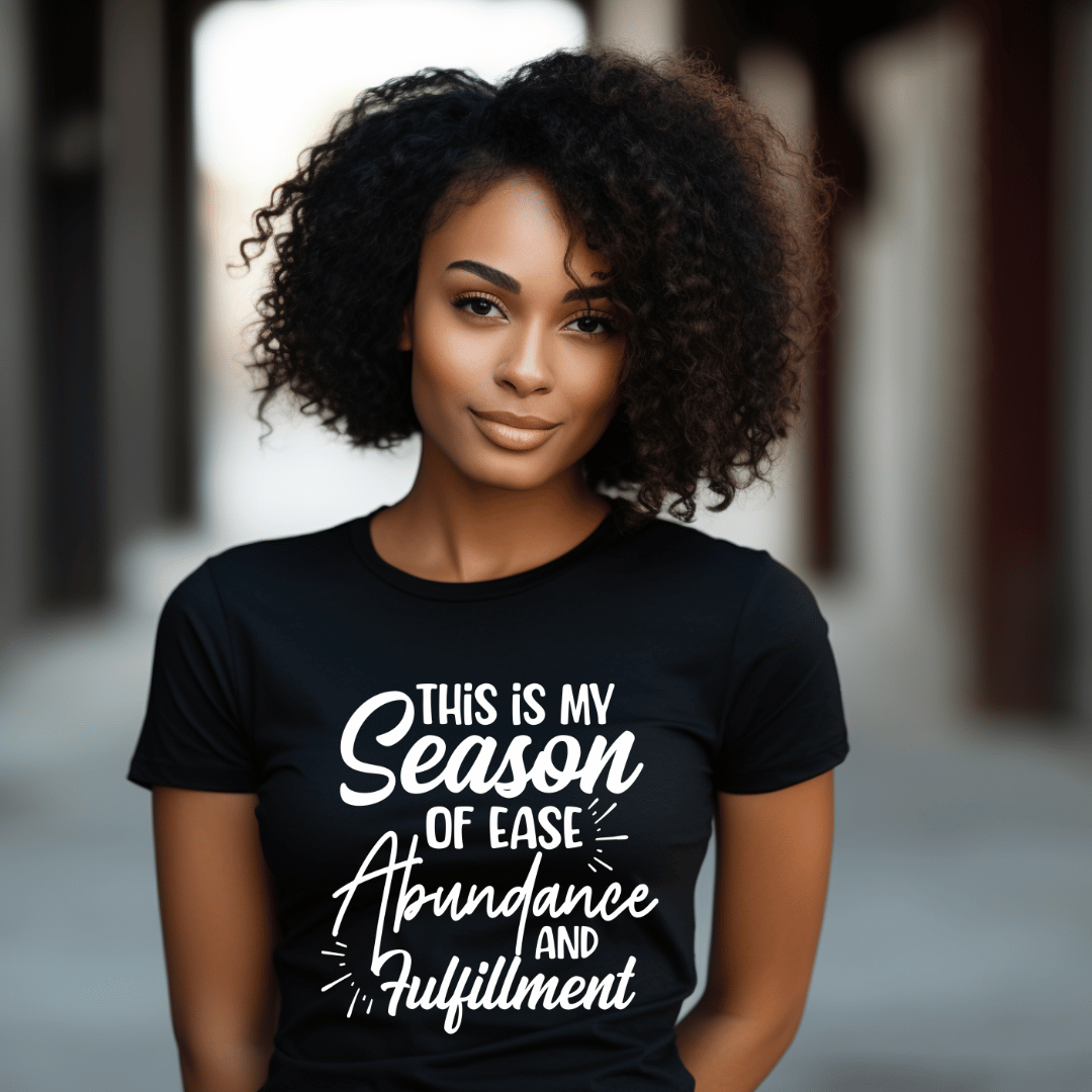 This **This is My Season of Ease, Abundance, and Fulfillment Tee** in black crew neck is perfect for the woman who's embracing her season of abundance. Designed by **Sharp Tact Kreativ**.