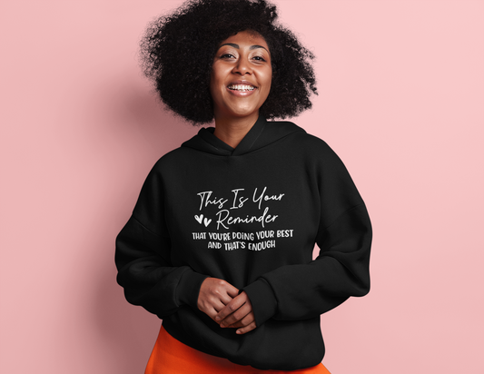A woman wearing a black hoodie with the Sharp Tact Kreativ This is Your Reminder that You're Doing Your Best and That's Enough Hoodie (heart) affirmation reminder.