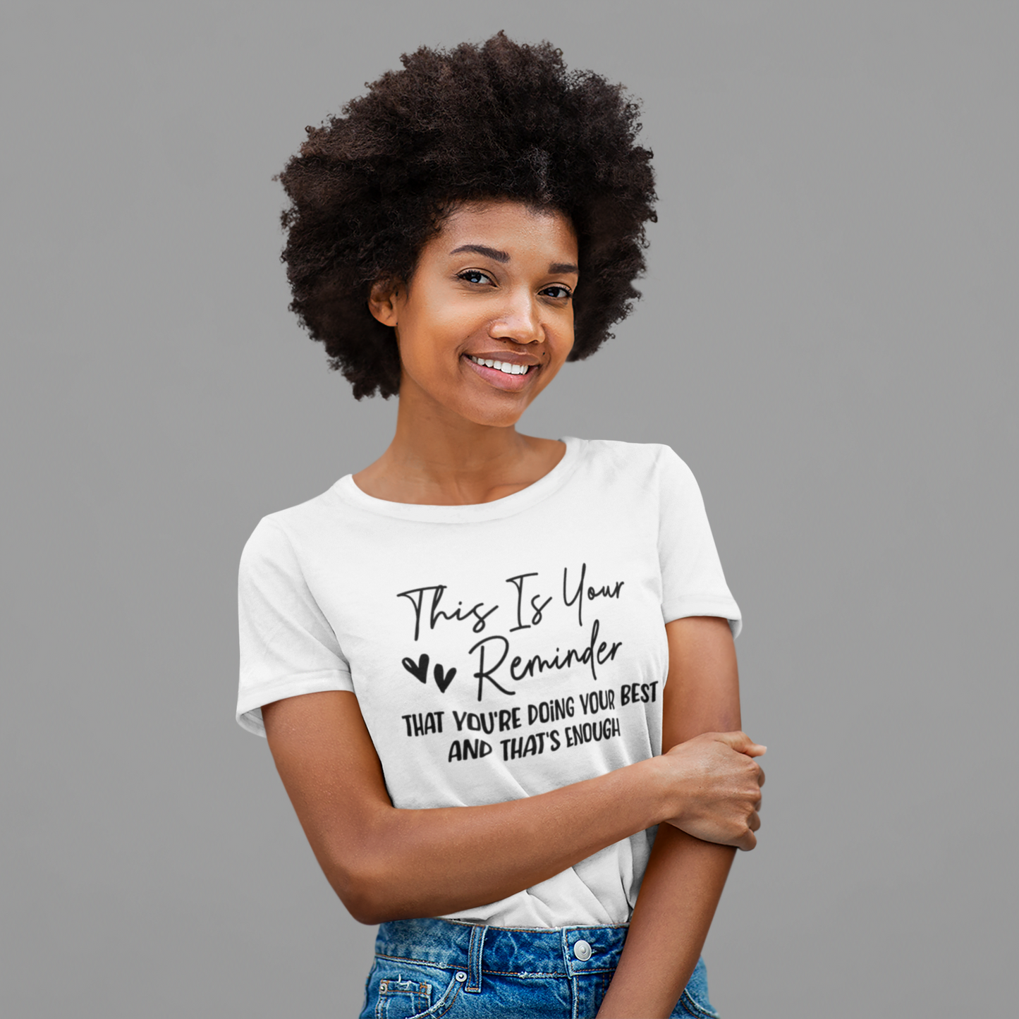 A woman wearing a white t-shirt that says "This is Your Reminder that You're Doing Your Best and That's Enough Tee (heart)" from Sharp Tact Kreativ | Tees & Gifts with Encouraging Messages to Brighten Your Day with a Bit of Wit.