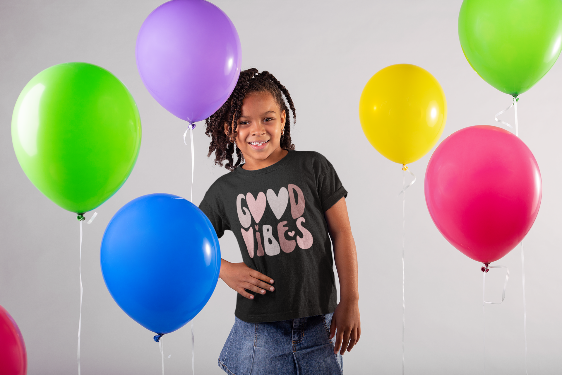 A little girl standing in front of balloons with the Sharp Tact Kreativ Good Vibes Tee (Youth Size).